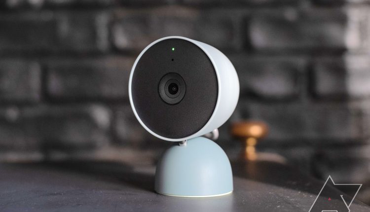A blue Google Nest camera in front of a black brick background.