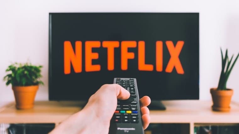 Netflix logo on a TV screen and a hand with a remote pointing to the TV