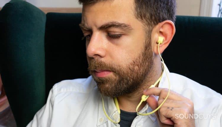A man wears the Beats Flex wireless earbuds in yellow.