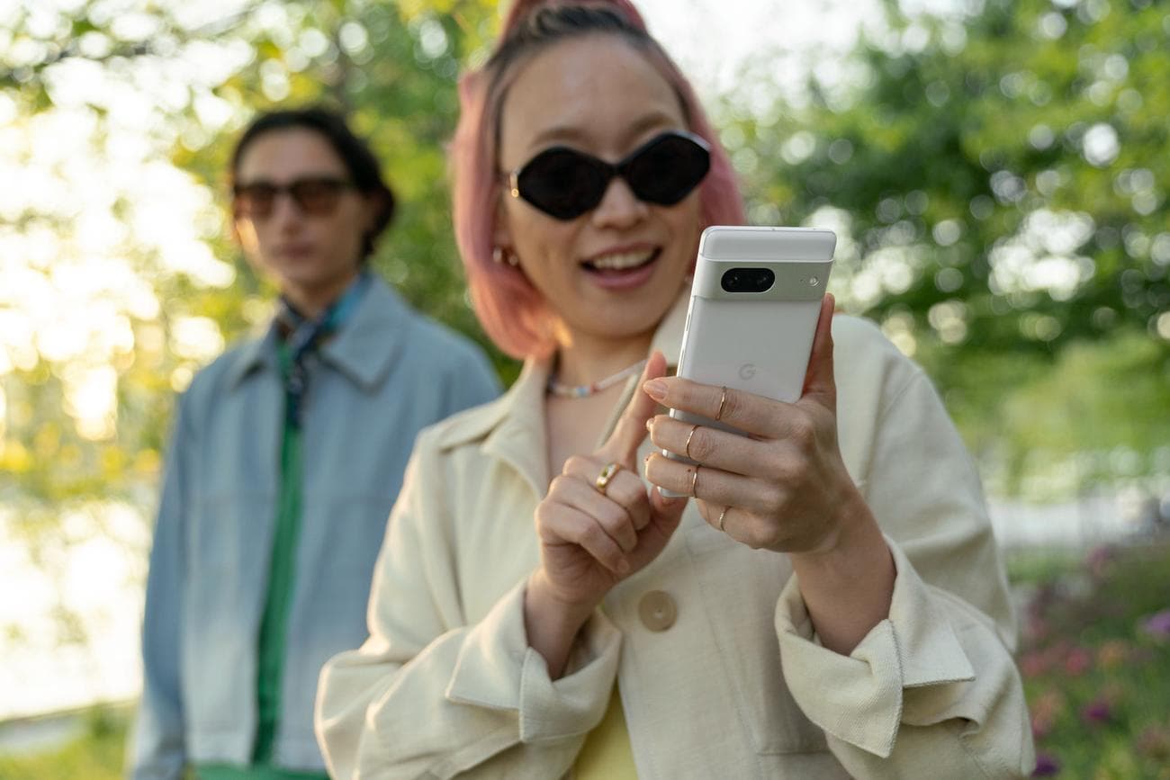 Ένα άτομο με κομψά ρούχα κρατιέται ψηλά και ετοιμάζεται να πατήσει την οθόνη ενός τηλεφώνου Android.  Είναι με άλλο άτομο και φαίνεται να είναι έξω σε ένα μονοπάτι στη φύση.