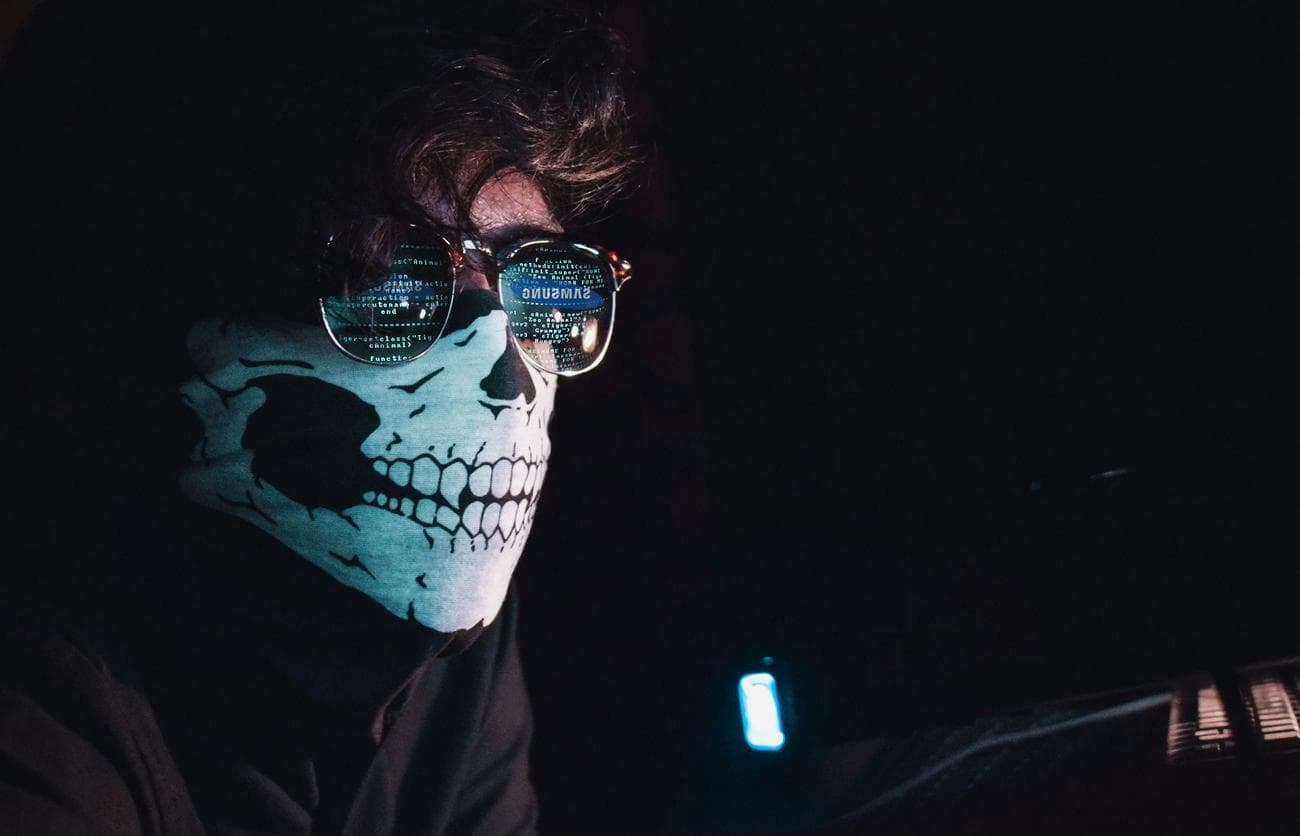 Μια εικόνα ενός ατόμου που φοράει μάσκα κάτω κρανίου μισού προσώπου και σκούρα γυαλιά.  Η αντανάκλαση στα γυαλιά δείχνει γραμμές κώδικα, που αντιπροσωπεύουν την έννοια της ανωνυμίας και την κρυφή φύση του σκοτεινού ιστού.