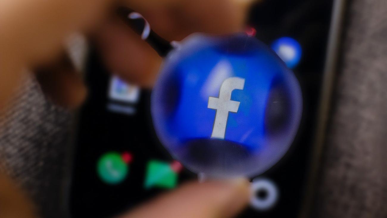 Person holding magnifying glass over Facebook icon