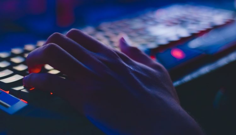 Image of a hand typing on a keyboard in a dimly lit room with a blurred background.