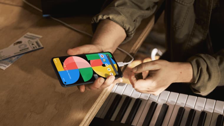 Ένα Google Pixel 5a 5G που κρατιέται πάνω από ένα πιάνο συνδεδεμένο σε ένα καλώδιο φόρτισης
