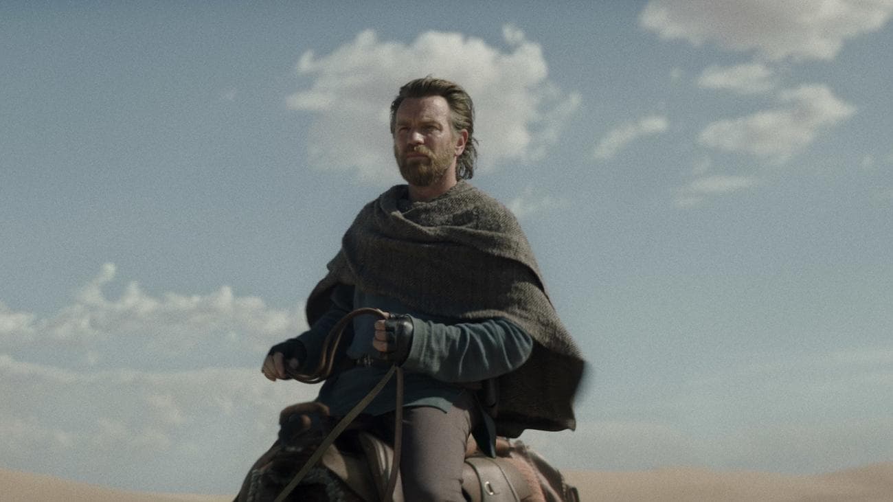 A man in linen sits on a camel-like animal in the desert