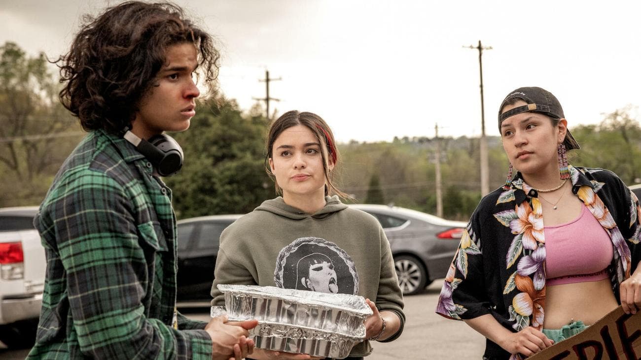 Three young people stand in a parking lot with two aluminum trays.