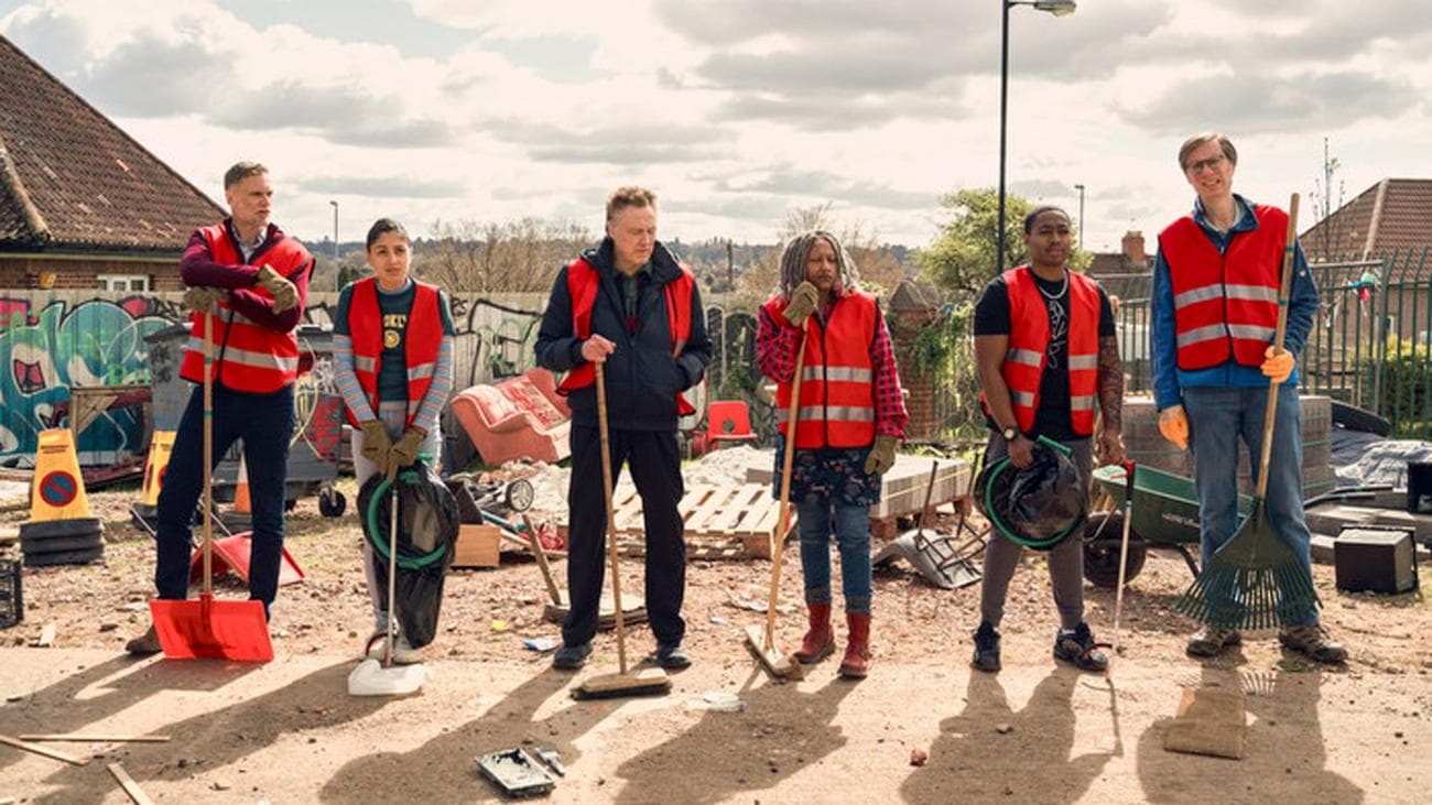 A group of people in hi-vis vests and trash spears stand in a line.