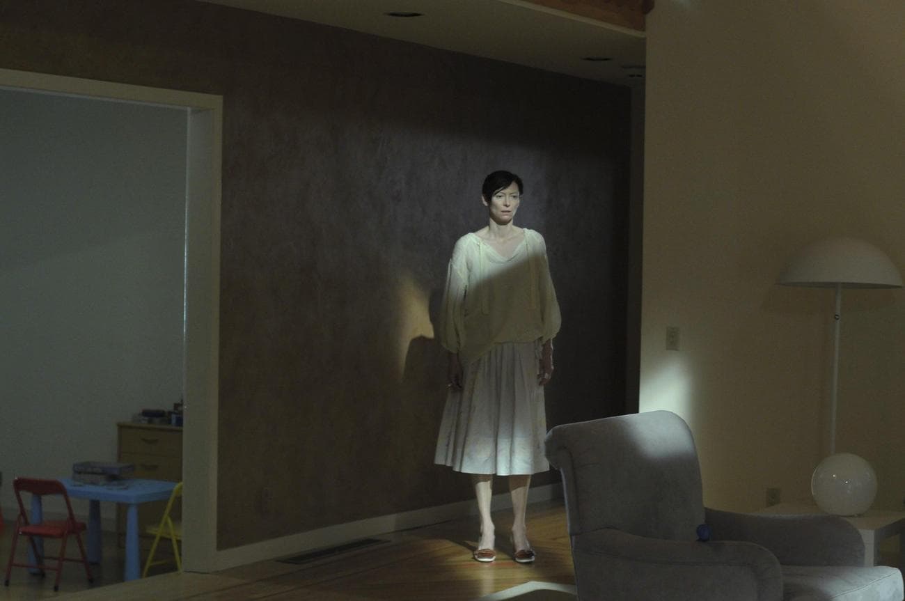 A woman stands in a room looking shocked, shaded in light and dark.