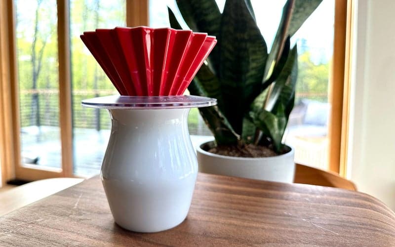 Red ceramic Origami pour-over dripper on a table with a snake plant