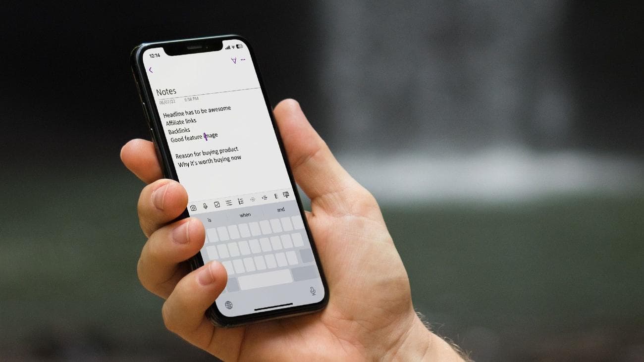 An iPhone held in a hand showing a screen of notes and the on-display keyboard