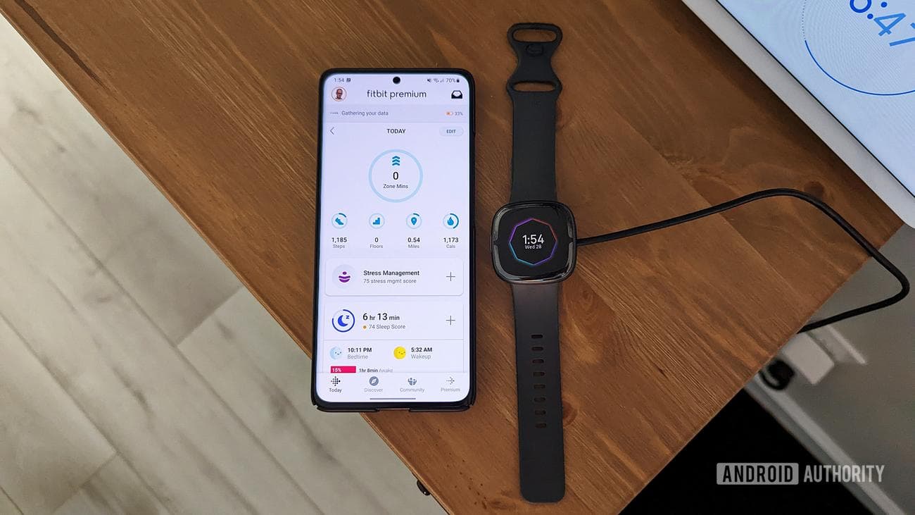 Ένα Fitbit Sense 2 βρίσκεται δίπλα στο τηλέφωνο ενός χρήστη που εμφανίζει την εφαρμογή Fitbit.