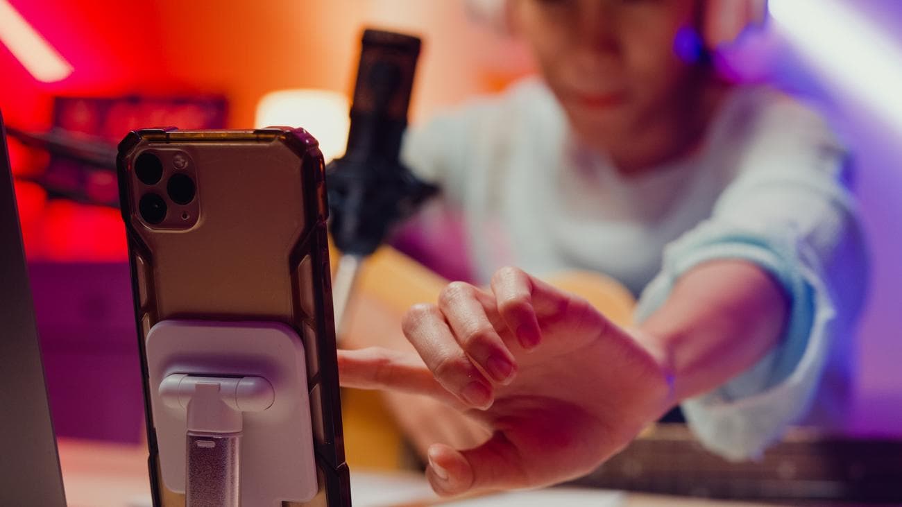 Κοντινό πλάνο Ευτυχισμένο κορίτσι από την Ασία, που φοράει ακουστικά επιρροής με δίσκο κιθάρας, podcast onair online live streaming, σχόλια ακολούθων και κοινό στο τηλέφωνο στο στούντιο στο σπίτι.