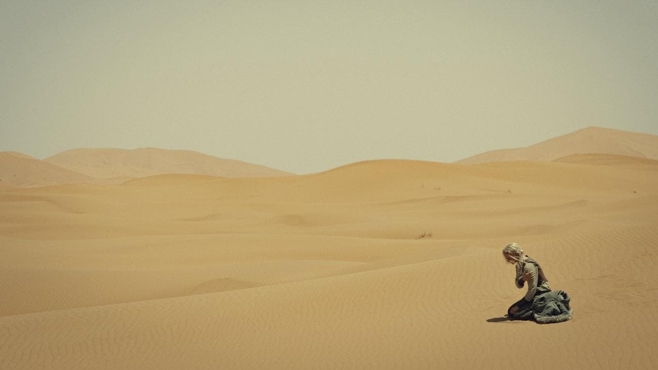 Freya Allan crouches alone in the desert in the show "The Witcher"