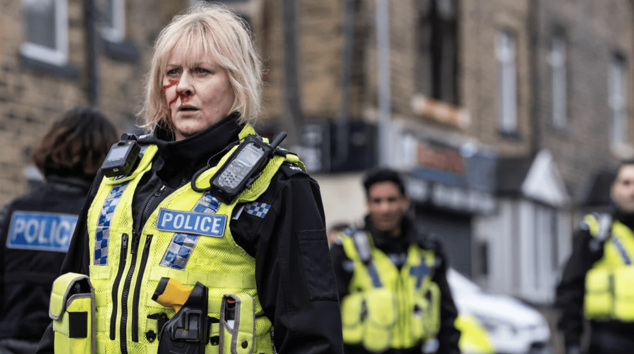 A police officer played by Sarah Lancashire stands in the street with blood on her face.