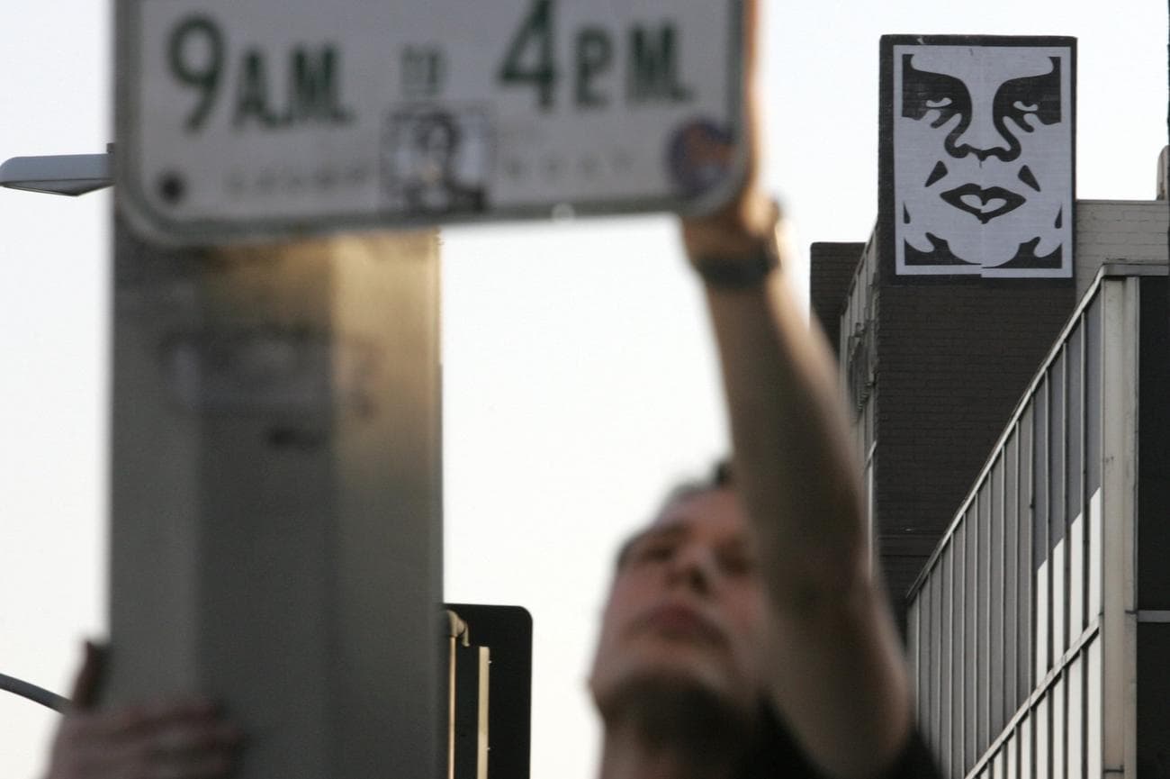 Artist Shepard Fairey puts a sticker on the back of a parking sign as his 