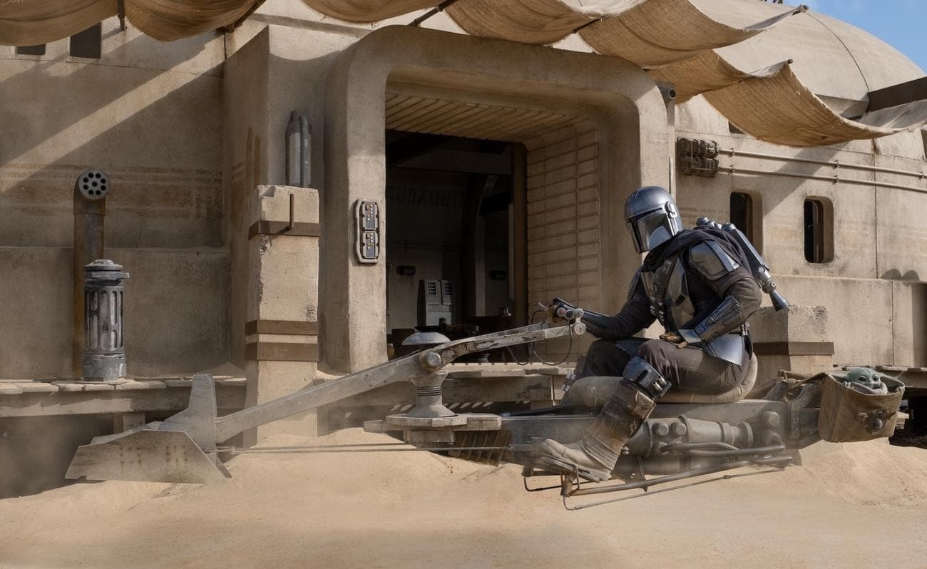 An image of the Mandalorian on a speeder bike with Grogu in a satchel