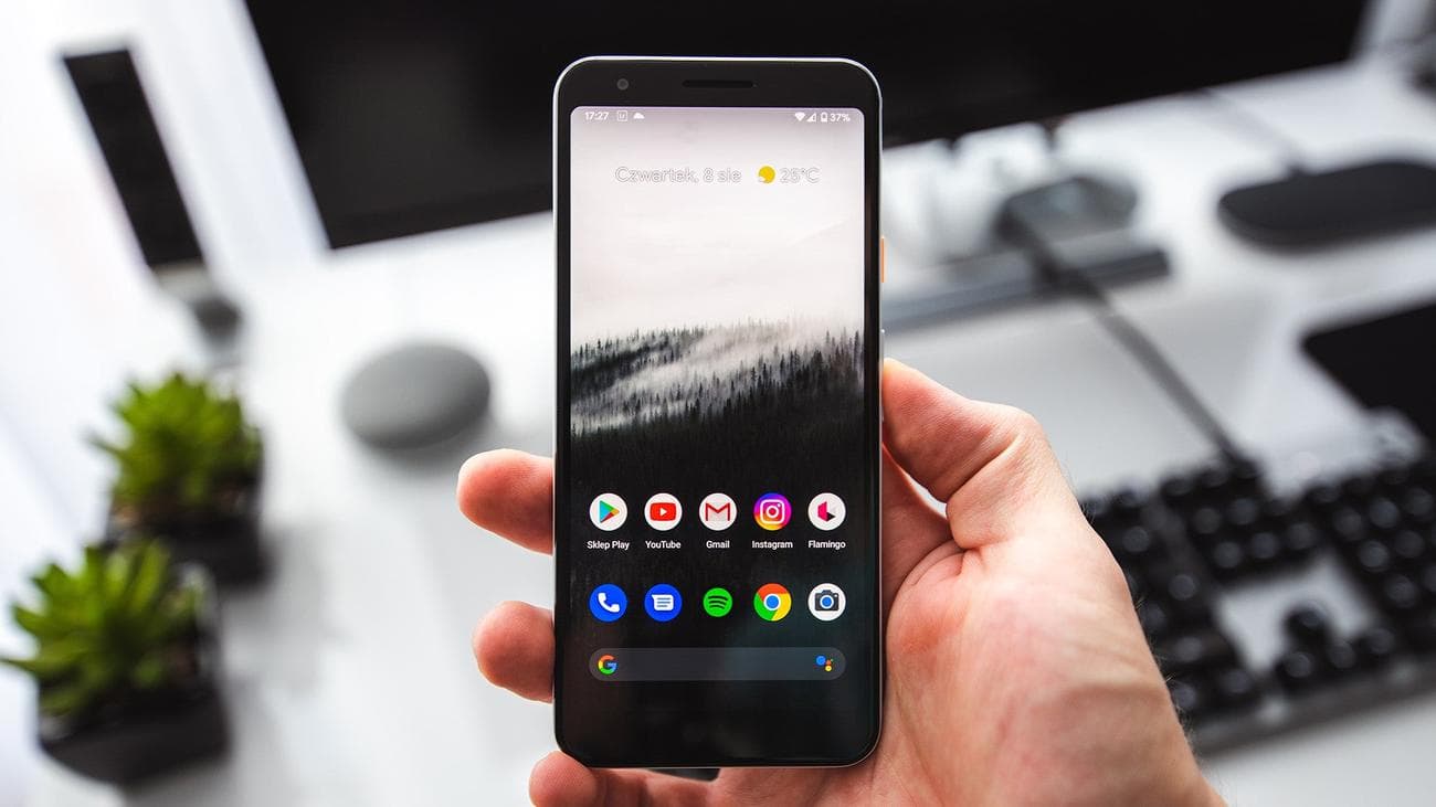 A hand holding a Pixel phone with the home screen unlocked.