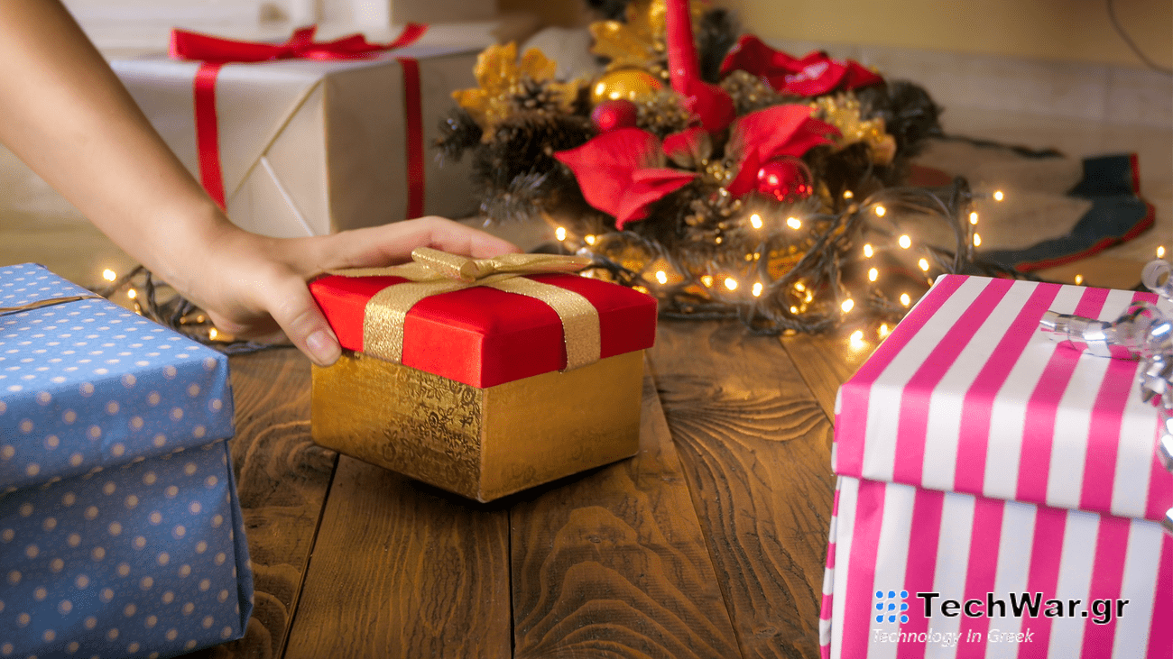 A hand reaches for a present wrapped in red and gold wrapping paper underneath a Christmas tree.