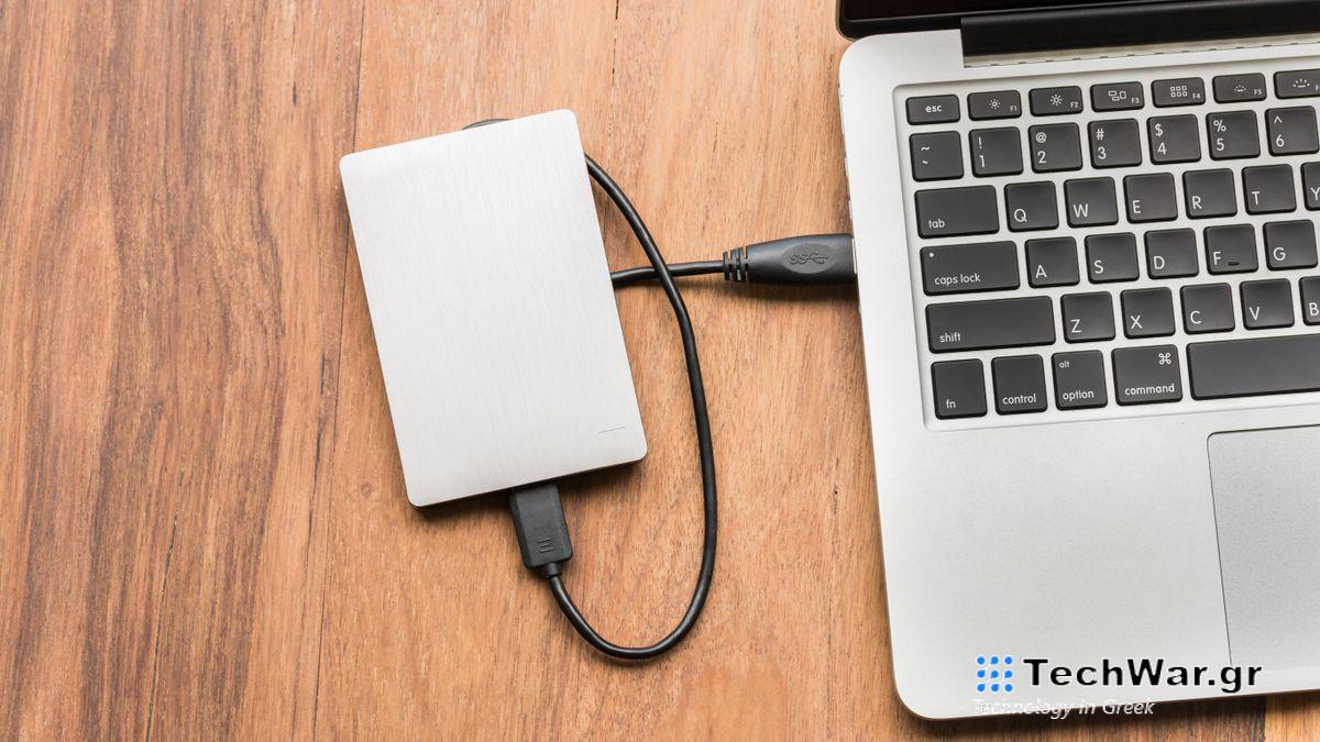 An image of an external hard drive with a brushed metal finish, plugged into a MacBook with a black USB cable
