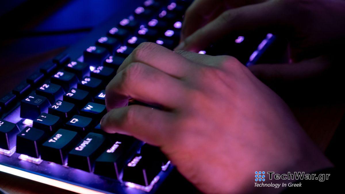 A person typing on a keyboard which has purple backlighting under the keys