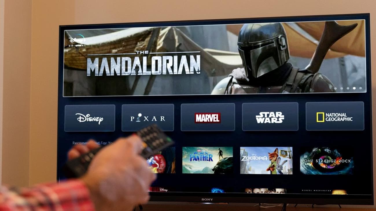 Χέρι με τηλεχειριστήριο μπροστά από την Disney Plus σε μια τηλεόραση