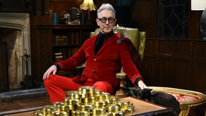 Η 2η σεζόν The Traitors είναι μια μεγάλη επιτυχία στις Alan Cumming sits next to a stash of gold coins in The Traitors US season 2 on Peacock