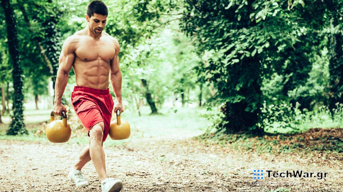 Man walking through a park holding two kettlebells performing a farmer
