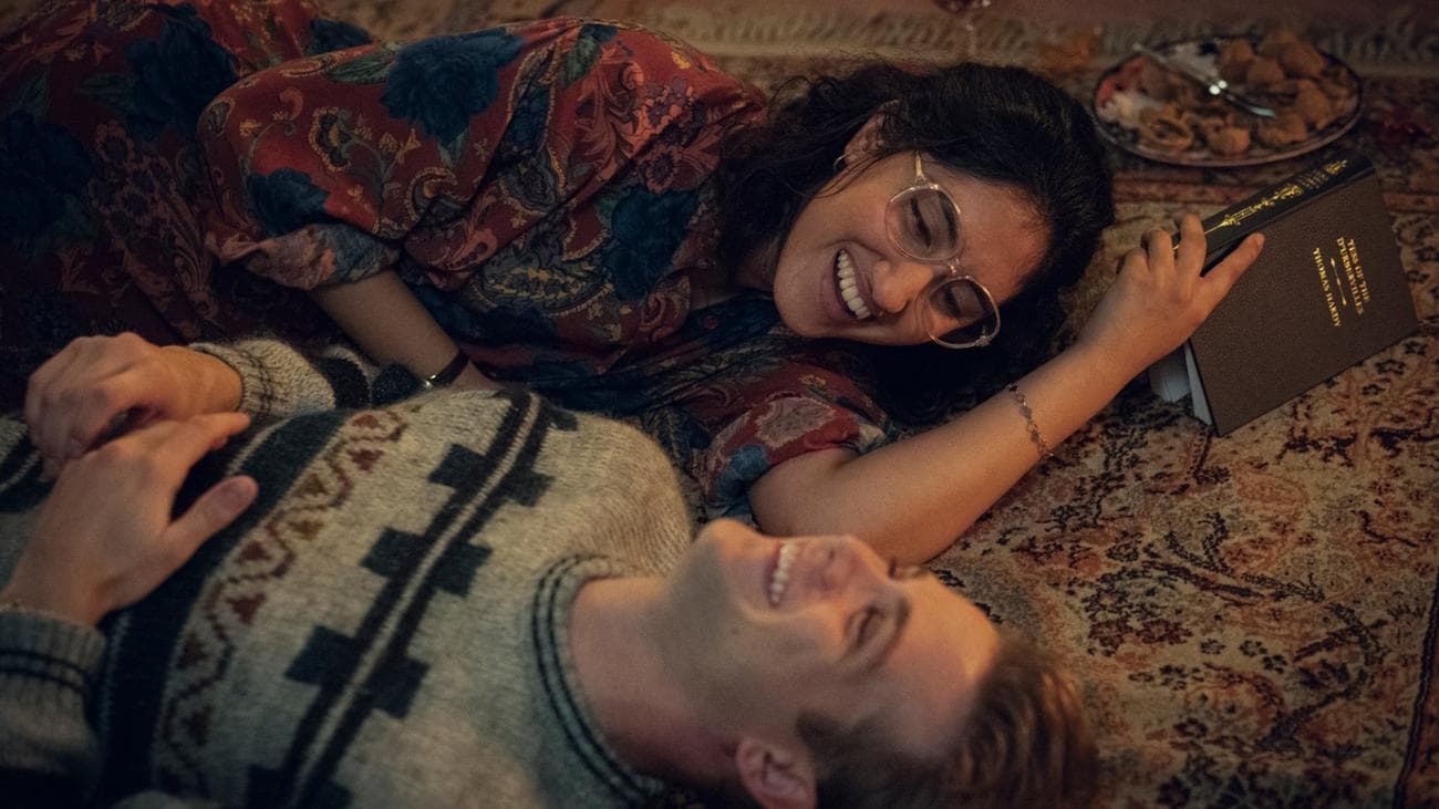 Μια νεαρή γυναίκα και ένας νεαρός άνδρας βρίσκονται γελώντας σε ένα χαλί διαβάζοντας ένα βιβλίο.