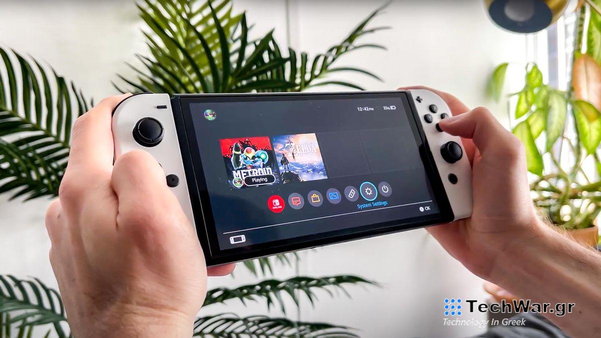 A pair of hands holding a Nintendo Switch showing the System Settings icon highlighted on the home screen.