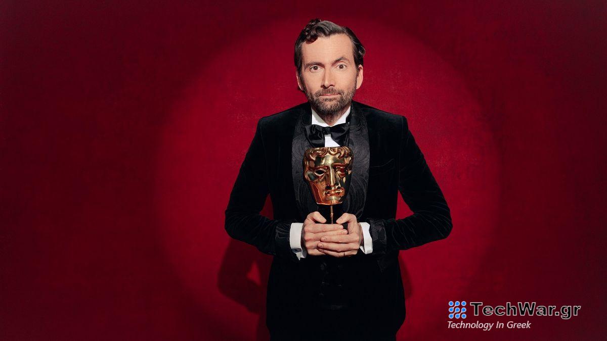 David Tennant in a suit holding a golden BAFTA trophy and standing in a spotlight in front of a red curtain