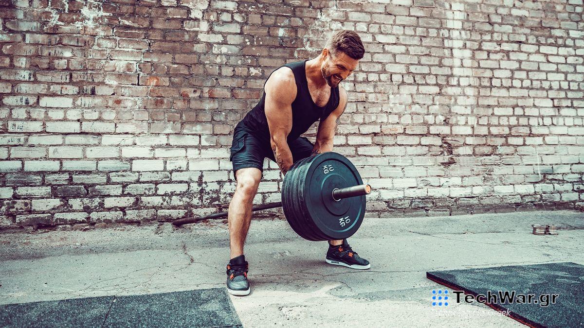 Man lifting a barbell with plates on using both hands during outdoor strength training session in yard