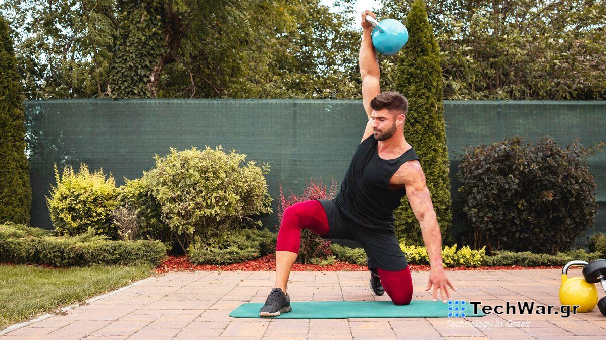 Man performing kettlebell workout in garden on yoga mat holding weight overhead in lunge position